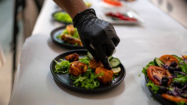 Bir şefin eldivenli eli salata ve limonlu siyah bir tabakta, Hint mutfağında özel bir restoranda servis edilecek tabakları hazırlayan tandır.