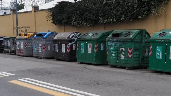 Bolonya, İtalya 7 Şubat 2025 Büyük yeşil ve gri çöp konteynırları Sırası Sarı duvarlı asfalt yol üzerinde Grafiti ve tırmanma bitkileri ile