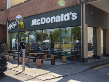 Lombardy, İtalya - 12 Mayıs 2025 İtalyan McDonald 's Sahnesi Dışarıda ahşap masa ve sandalyelerle güneşli bir gün, İnsanlar yemeğin keyfini çıkarıyor, yakınlarda arabalar park ediyor ve rahat bir atmosfer