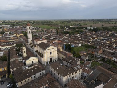 Kuzeydeki terasotta çatıları ve Pontevico tarihi merkezinin pencereleri üzerinde, Abbazia dei Santi Tommaso ve Andrea Apostoli 'nin ince çan kulesi şehir ağaçlarının tepesinde.