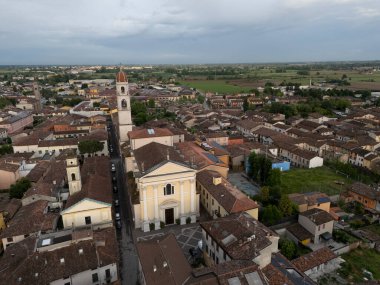 Kuzeydeki terasotta çatıları ve Pontevico tarihi merkezinin pencereleri üzerinde, Abbazia dei Santi Tommaso ve Andrea Apostoli 'nin ince çan kulesi şehir ağaçlarının tepesinde.