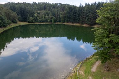 Meugliano Gölü 'nün düşük hareketli insansız hava aracı manzarası Val di Chy' de yoğun kozalaklı ağaçlarla çevrili, Ivrea Morainic Amfitiyatrosunun bir parçası, Kuzey Piedmont 'ta tarih öncesi bir buzul arazisi, insansız hava aracı atışı