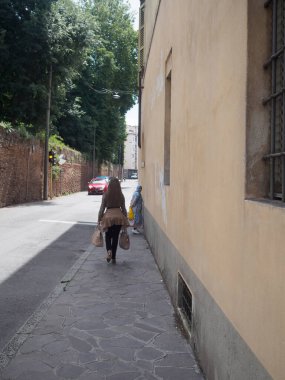 Cremona, İtalya 11 Haziran 2025 Dar Bologna caddesinde alışveriş torbaları taşıyan şık bir kadın, Müslüman kadınlar taş duvarın karşısında sohbet ediyorlar