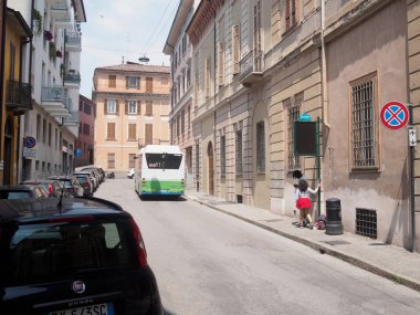 Cremona, İtalya 11 Haziran 2025. İki genç öğrenci otobüslerini İtalyan kasabasının dar bir sokağında, otobüs durağında bekliyorlar.