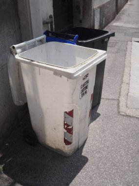 Cremona, İtalya 11 Haziran 2025 Beyaz çöp kutusu kaldırımda siyah bir çöp kutusunun yanında duruyor, içinde kağıt ve karton geri dönüşüm etiketi var.