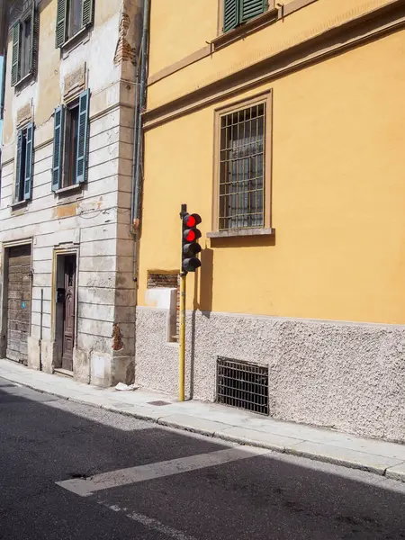 Cremona, İtalya 11 Haziran 2025 güneşli bir günde kaldırımda duran kırmızı trafik ışığı, eski binalar, pencereler ve gölgeler bir İtalyan şehrinde bir caddenin asfaltında yansıtılıyor.