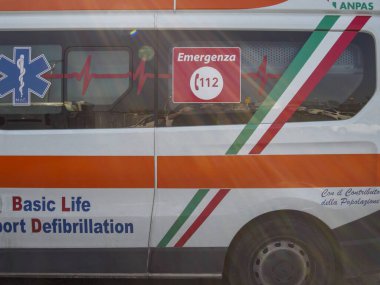 Cisanello, PI, İtalya - 13 Haziran 2025 Bir İtalyan ambulansının yanına yansıyan güneş ışığı, acil durum numarası 112, Yaşam Yıldızı, temel yaşam desteği ve defibrilasyon işaretleri ve