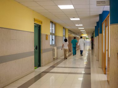 Cisanello, PI, İtalya - 13 Haziran 2025 hastane koridoru sahnesinde doktorlar ve hemşireler kapalı kapılar ve duvarlarla uzun bir koridorda yürürken, tıbbi alanda tipik bir iç dekorasyon sergiliyorlar.