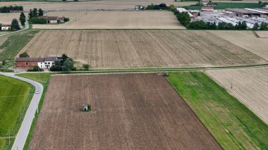 Havadan çekilen görüntüler çiftçinin verimli tarlaları sürdüğünü gösteriyor, tarımsal yaşam tarzını tasvir eden geniş pastoral arazinin ortasında yıpranmış çiftlik evinin yakınındaki kırsal yol kıvrımları