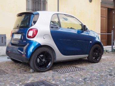 Cremona, İtalya 11 Haziran 2025 Açık mavi ve gümüş renkli üç çeyrek görünüm Smart ForTwo MHD, parke taşı bir cadde üzerinde ahşap kapılı bir bina önünde park
