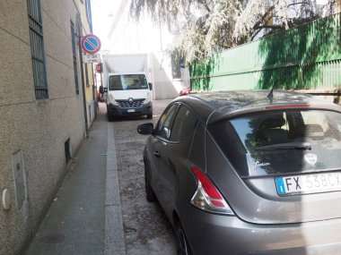 Cremona, İtalya 11 Haziran 2025 Gri metalik Lancia Ypsilon Duyguları 1.2 beyaz bir Renault Master 'ın yanına park etmiş Milano, İtalya' da dar bir sokakta, park işareti olmadan.