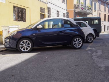 Cremona, İtalya 11 Haziran 2025 Koyu mavi Opel Adam 1.4 EKOFLEX beyaz bir Fiat 500 ve yeşil bir Land Rover Defender 'ın yanına park etmiş güneşli bir yaz gününde