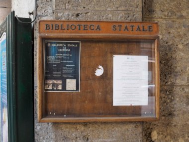 Cremona, İtalya 15 Haziran 2025 Kütüphane bilgilerini gösteren tahta tabela, Biblioteca Statale di Cremona yakınlarındaki tarihi taş duvara yapıştırılmış, operasyonel ayrıntılar ve ziyaretçi guida