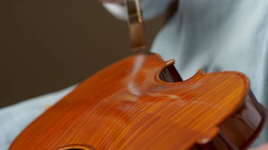 Luthier atölyesinde el yapımı bir kemanı titizlikle cilalıyor, koruyucu bir katman için fırça kullanıyor, karmaşık ahşap tahıl ve işçiliğini sergiliyor.