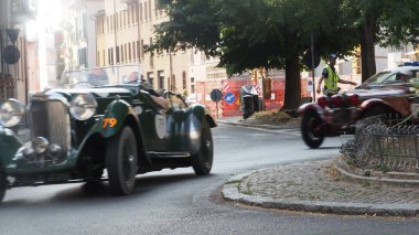 Cremona, İtalya 21 Haziran 2025 Mille Miglia 2025 'te Cremona caddelerinde hız yapan iki klasik araba, prestijli bir klasik araba yarışı, bir polis ise trafiği yönetiyor.