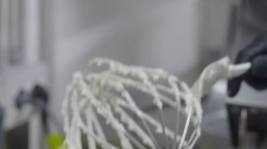 Beyaz kremayla kaplı çırpıcıyı kapat, siyah eldiven giyen bir pasta şefi tarafından, profesyonel bir mutfak ortamında, lezzetli bir tatlı hazırlamak için