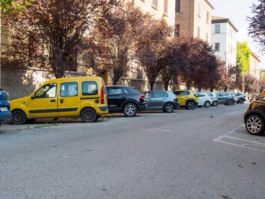 Bologna, İtalya 3 Temmuz 2025 Kalabalık toplu konut parkı, sarı Renault Kangoo dar kentsel mahallede yapraklı arka planda.
