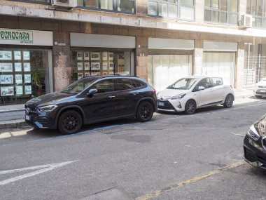 Bologna, İtalya 3 Temmuz 2025 Siyah Mercedes Benz GLA ve beyaz Toyota Yaris İtalya 'da bir şehir caddesinde bir emlak acentesinin önündeki paralı bir park yerine park ediyorlar.