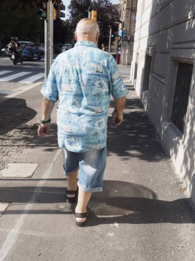 Bolonya, İtalya 3 Temmuz 2025 Bologna kaldırımında yürüyen, renkli Hawai gömleği giyen, parlak yaz öğleden sonra dinlenen, kaygısız emeklilik yaşam tarzını somutlaştıran yaşlı vatandaş.