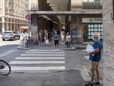 Bologna, İtalya 3 Temmuz 2025 Dar Bologna caddesinde duran son sınıf öğrencisi, gazete okuyor, eski bisikletler güneşli havada tarihi bina duvarına yaslanırken yayaları seyrediyor.