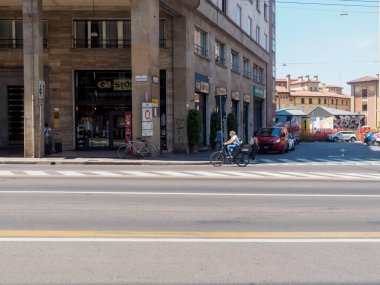 Bologna, İtalya 3 Temmuz 2025 tarihi Bolonya 'da bisiklet süren bir kadın, yaz öğleden sonra sıcak güneş ışığı altında tarihi binalar ve mağazaların önünden geçiyor.