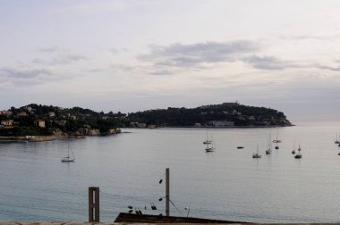 Kaptan Ferrat, Fransa - 1 Ocak 2010 'da Fransız Rivierası' nın manzaralı bir kasabası olan Villefranche sur Mer 'deki Kaptan Ferrat yakınlarında bulutlu bir gökyüzünün altında huzurlu bir deniz manzarası yaratarak yüzüyorlar.