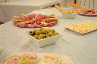 Beyaz bir masa örtüsü üzerinde güzel bir aperatifler ve pişirilmiş etler. Zeytinli peynirli ekmek çubukları ve çeşitli mezeler içeren her etkinlik için enfes bir mutfak sunumu.