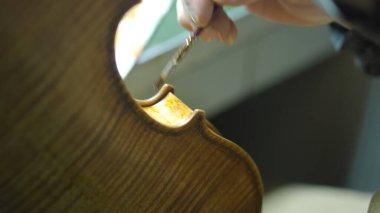 Luthier titizlikle bir kemanı fırçayla cilalıyor, yeni enstrümana doğal güzelliğini artırırken eski ve kaliteli bir görünüm kazandırmak için ustaca bir antika tekniği uyguluyor.