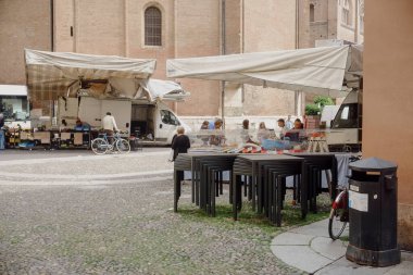 Cremona, İtalya - 1 Nisan 2025 Tezgâhlarını İtalyan meydanındaki hareketli bir çiftçi pazarında düzenleyen satıcılar, tarihi bir kilisenin yakınlarındaki hevesli müşterilere taze ürünler ve yerel ürünler sunuyorlar.