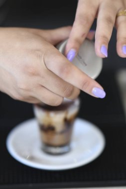 Cremona, İtalya - 21 Temmuz 2025 Bir baristanın yakınına dikkatlice beyaz bir fincan çay tabağındaki cam bardağın içindeki özel bir kahve bardağının tepesini ekle