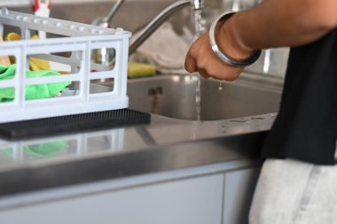 Cremona, İtalya - 21 Temmuz 2025 Modern bir mutfak lavabosunun musluk suyunun altında temizlik ve temizlik kavramı için arka planda bulaşık kurutma askısı bulunan bir kişinin ellerinin yakın çekimi