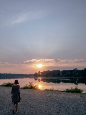 Yalnız Kadın, San Nazzaro 'da Serene Po Nehri' ne doğru yürüyor. Berrak Yeşillikler ve Uzaktaki Ağaçlar arasında Sakin Su Üzerine Altın Renkler Yansıtıyor.