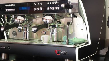 Cremona, İtalya - 26 Temmuz 2025 Buharlı üç grup espresso makinesi ve sıcak su dağıtıcısı küçük beyaz bir fincan kahve hazırlıyor