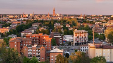 İtalya 'nın Cremona kentinin ikonik Torrazzo çan kulesinin günbatımının sıcacık parıltısıyla aydınlatıldığı hava manzarası binaların ve yeşilliklerin manzarası.