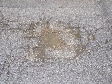 Çatlak asfaltın soyut dokulu arka planını granüler toprak ve yüzeydeki kusurları ortaya çıkaran küçük taşlarla kapat ve aşınma şekilleri hafif bir sıkıntı yaratıyor.