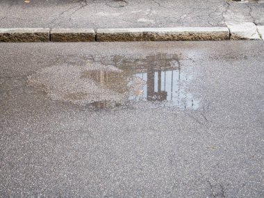Yağmurdan sonra asfalt yol yüzeydeki bir su birikintisinde sokak ışığı yapısının net bir yansımasını gösteriyor.