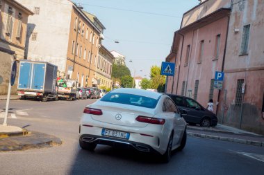 Cremona, İtalya 6 Ağustos 2025 Modern beyaz Mercedes Benz E sınıfı Coupe dar bir caddede italyan şehir bağlamında sürüyor, diğer araçlar yol kenarına park edilmiş.