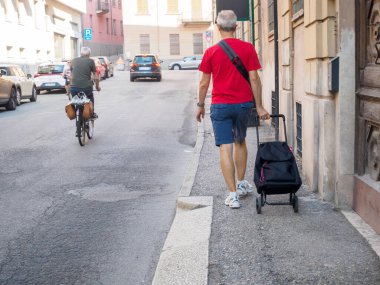 Cremona, İtalya 6 Ağustos 2025 Yaşlı Yaşlılar alışveriş arabasıyla yürürken, refakatçi bisikletler Cremona, Lombardy 'de, yaşlı vatandaşlar mahallede dolaşıyorlar.