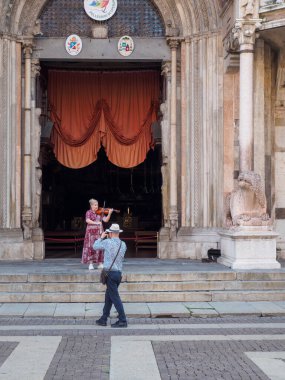 Cremona, İtalya 6 Ağustos 2025 'te İtalya' nın Lombardy kentinde tarihi Cremona Katedrali yakınlarında sahne alan sokak müzisyenlerini fotoğraflayan turist.
