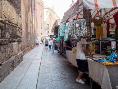 Cremona, İtalya. 6 Ağustos 2025. Sokak satıcısı. Canlı giysiler sergiliyor. Günışığı Cremona, Lombardy, tarihi İtalyan sokak manzarasında.