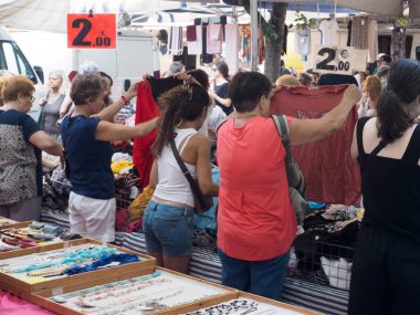 Cremona, İtalya - Lombardy İtalya 'da 6 Ağustos 2025 Vibrant sokak pazarı güneşli bir günde çeşitli müşterilerin giysi ve aksesuarlarını gezdiğini gösteriyor