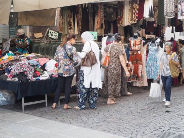 Cremona, İtalya - 6 Ağustos 2025 Lombardy İtalya 'daki Vibrant caddesi manzarası çeşitli giyim sergileri ve alışverişçiler yerel sanatsal eşyalar ve giyim seçimleri keşfediyor