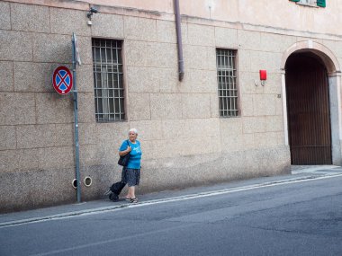 Cremona, İtalya 6 Ağustos 2025 Cremona, Lombardiya 'da yaşlı bir kadın, park levhası ve parmaklıklı pencerenin yanında, Cremona, Lombardy' de bir caddenin kaldırımında yürüyor.