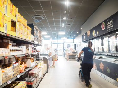 Cremona, İtalya - 28 Temmuz 2025 Bir bayan çalışan, güneşli bir günde parlak tavan lambaları altında, alışveriş yapan kişi rafları karıştırırken bir market koridorunda bir el arabasını itiyor.