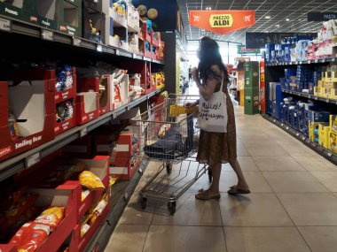Cremona, İtalya 11 Ağustos 2025. Genç bir kadın alışveriş arabasını itiyor ve çeşitli ürünlerle çevrili bir ALDI süpermarketinin tıka basa dolu koridorunda atıştırmalıkları seçiyor.