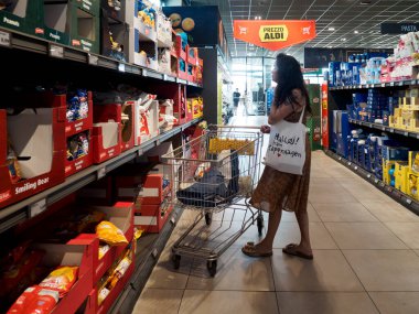Cremona, İtalya - 11 Ağustos 2025 İtalya 'daki parlak bir modern ALDI süpermarket koridorundaki indirimli sebzeleri dikkatlice seçen kadın haftalık alışverişi için yiyecek seçiyor.