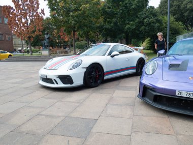 Cremona, İtalya 22 Ağustos 2025 İki Porsche 911 spor arabası, biri beyaz Martini Yarış Ahırı, diğeri mor, İsviçre 'nin Zug kentindeki kaldırımlı bir meydanda park edilmiş,