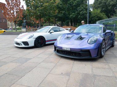 Cremona, İtalya 22 Ağustos 2025 Mor Porsche 911 GT3 RS 'nin yanında yürüyen bir kadın beyaz bir Porsche 911 GT3' ün yanında Martini eşliğinde, İtalya 'nın Varese kentindeki bir meydanda park edilmiş bir araba toplantısında