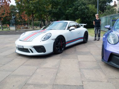Cremona, İtalya 22 Ağustos 2025 Beyaz Porsche 911 GT3 Martini Yarışı tarihi anıtın yanına park edilmiş, yarış meraklısı park yerinde parlayan ikonik spor arabaya bakıyor