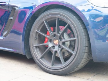 Cremona, İtalya 22 Ağustos 2025 Kırmızı fren kalibresi ve Porsche logosu ile gri alaşımlı bir tekerleğe yakın asfalt zemine park edilmiş mavi bir Porsche 718 Cayman 'a ait.